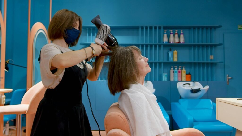 Hairdresser styling senior woman's hair with blow dryer in chic salon setting.