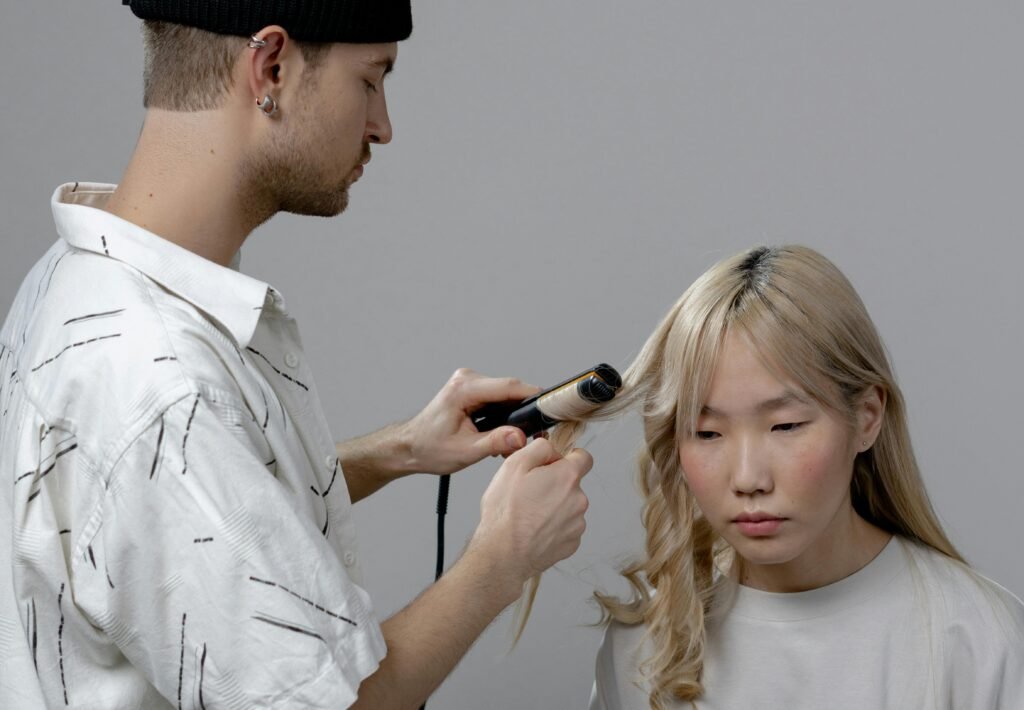 A hairstylist using a curling iron to style a woman's hair in a salon setting.